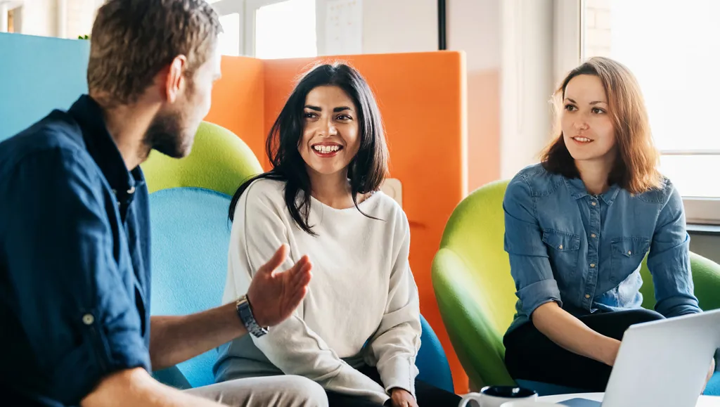 Mann med ryggen til prater engasjert med to kvinner i et arbeidsmiljø