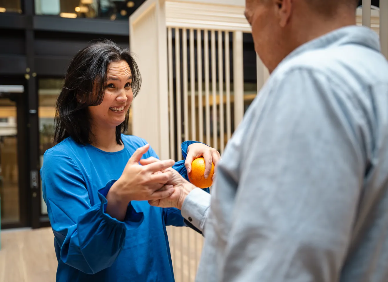 Kvinne som holder en appelsin i en hånd, og håndhilser på en annen person på en merkelig måte med den andre hånda