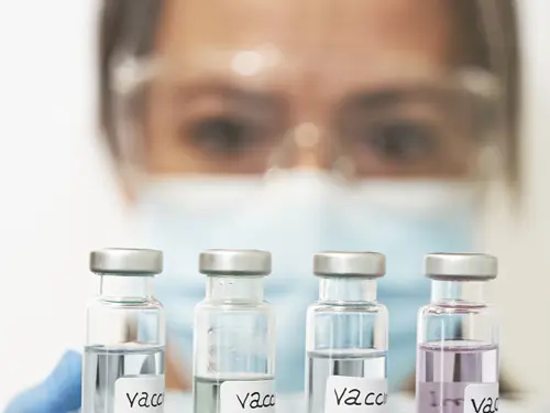 Nærbilde av en kvinne i verneutstyr i labor med reagensglass