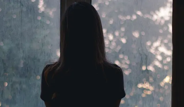 Person sett bakfra stirrer ut et regnfylt vindu