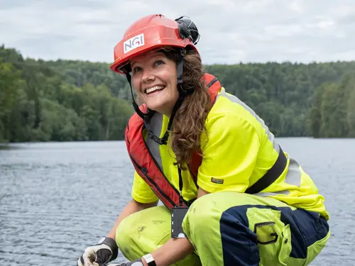 Dame i arbeidsdress, skrur på noe ved et vann