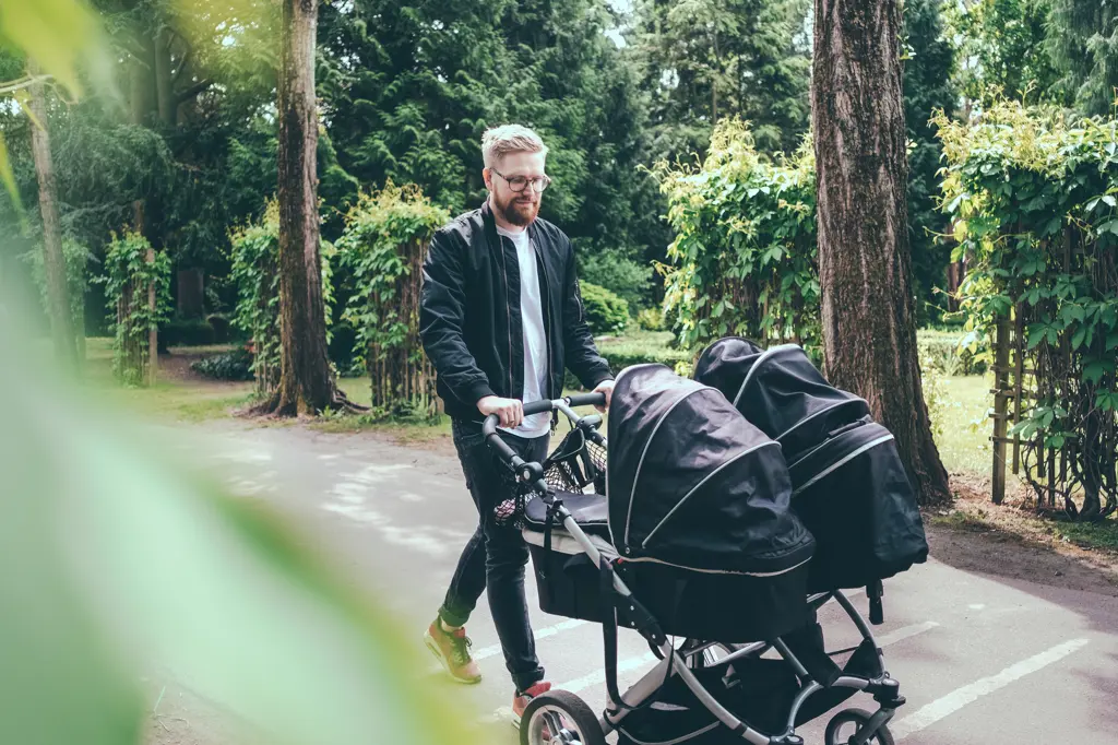 Mann triller barnevogn langs en park