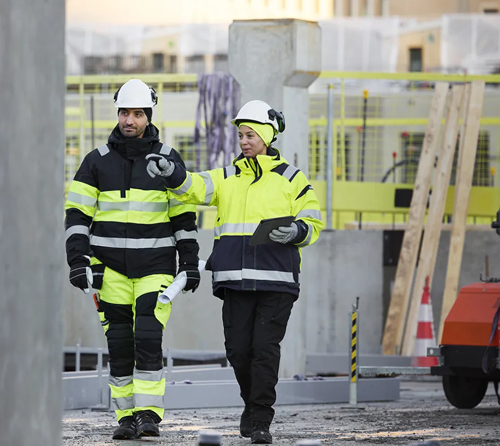 En mann og en kvinne i refleksklær på en byggeplass, som samarbeider om betongarbeid.