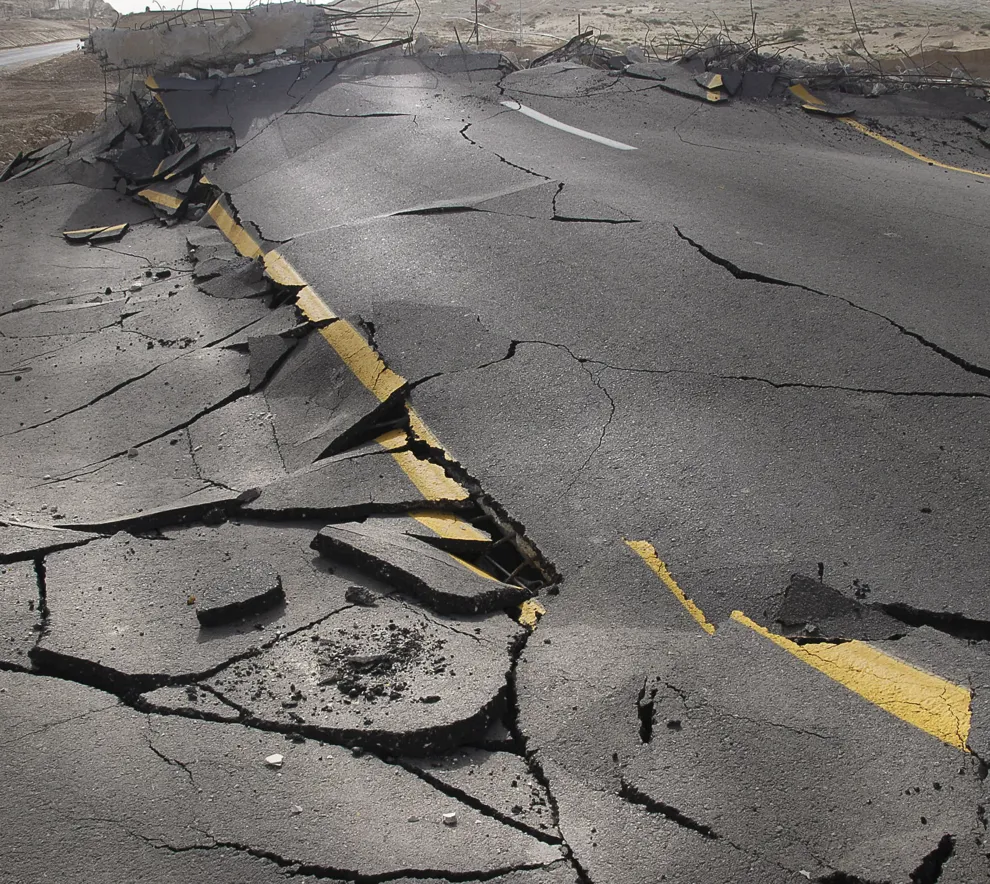 Veiskade etter jordskjelv med oppsprukket asfalt og gul midtstripe som er bøyd.