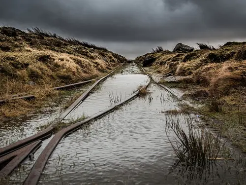 En oversvømt jernbane på en øde mark, stormfulle skyer i bakgrunnen.