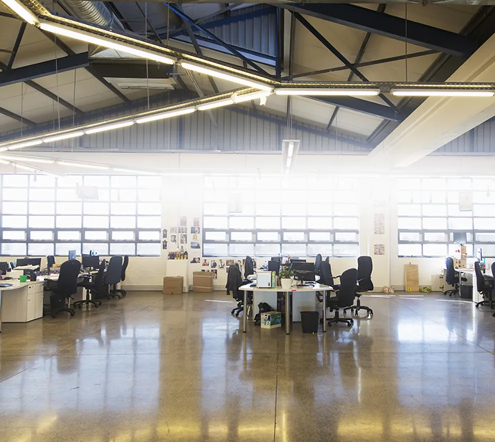 Et bredt perspektiv av et stort, åpent kontorlandskap med skarpt lys fra vinduer og taklys.