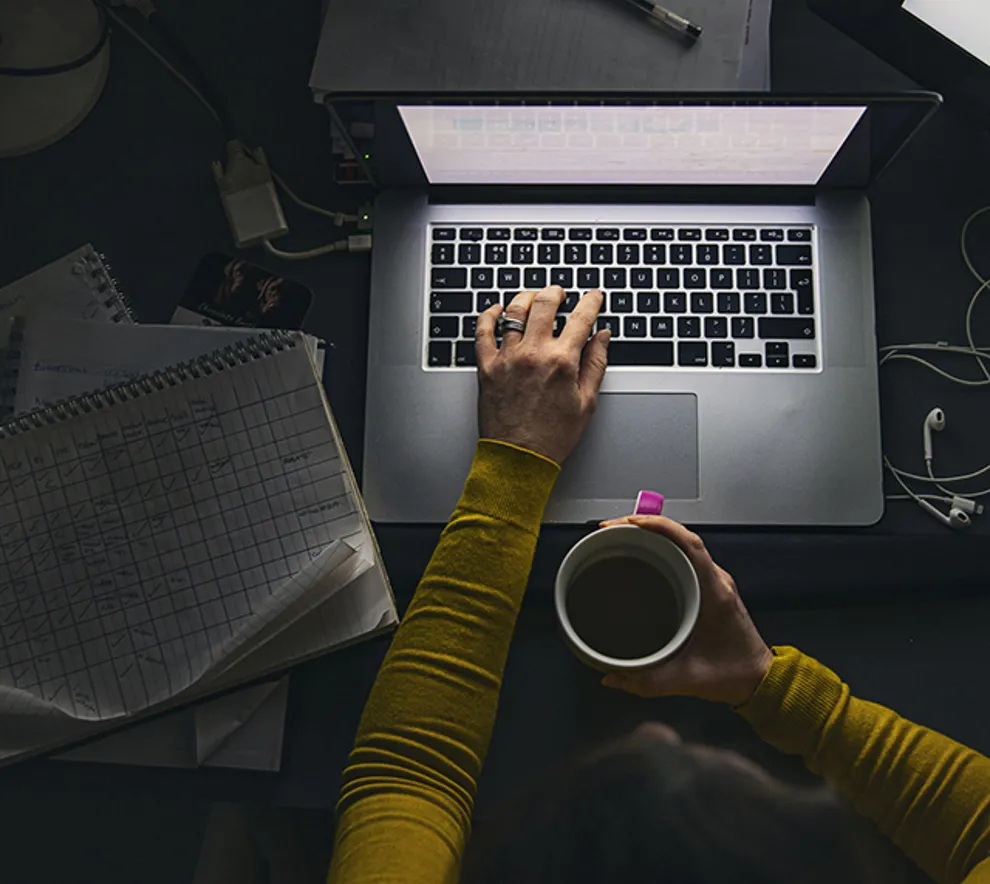 Kvinne jobber sent med laptop, omgitt av notater og kaffekopp – illustrerer arbeid, fokus og multitasking.