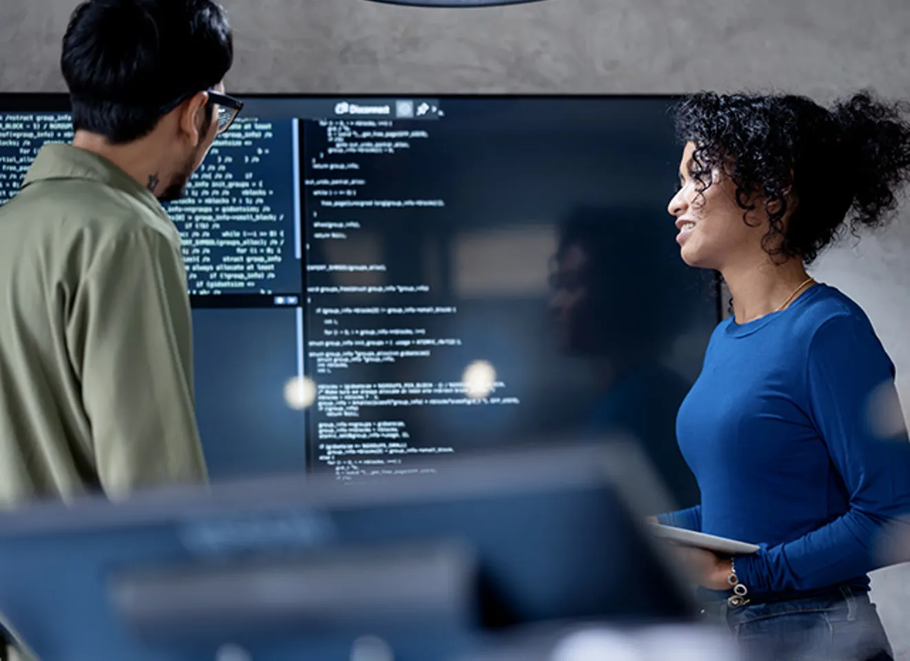 To utviklerkolleger diskuterer et prosjekt med skjermer rundt seg.