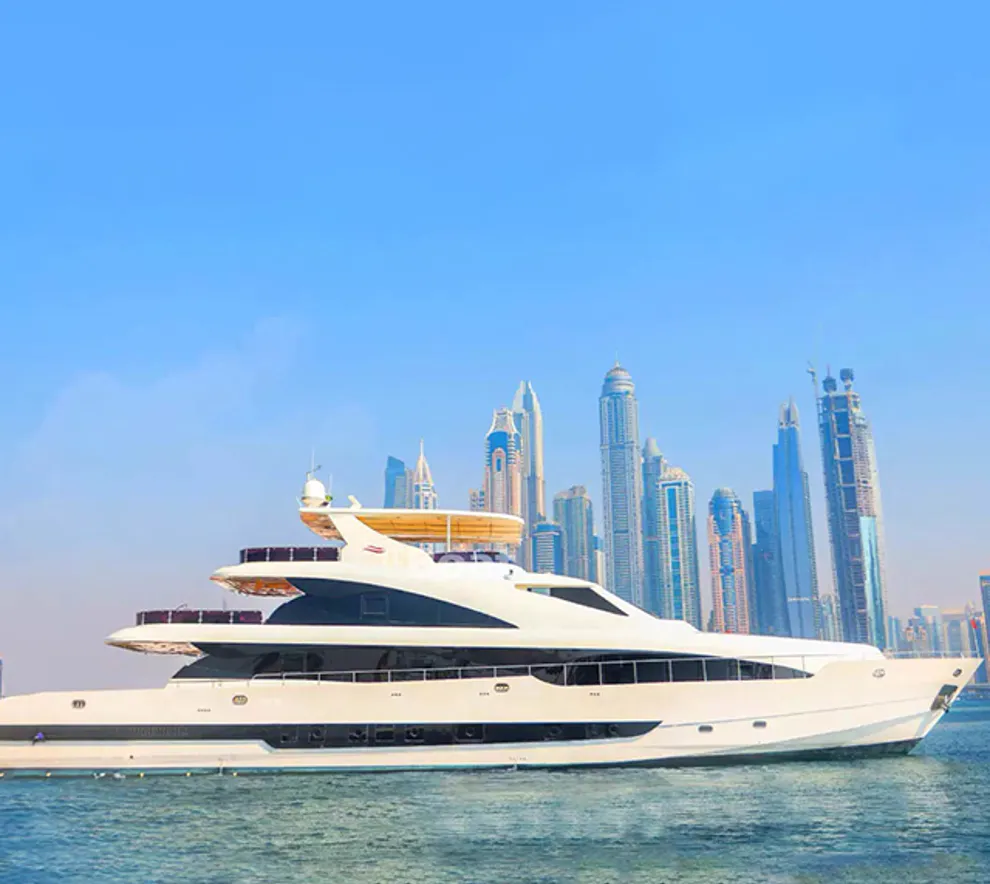 En yacht ligger i turkist vann med Dubais skyskrapere i bakgrunnen.