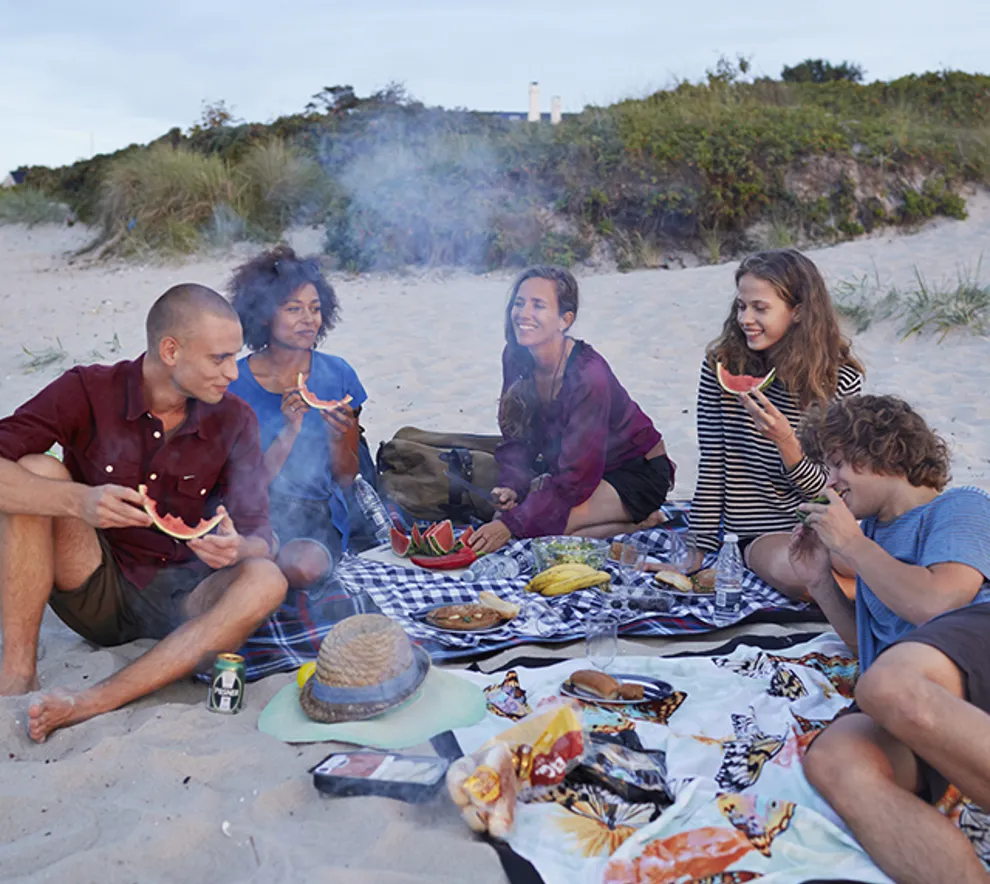 En gruppe mennesker griller og koser seg på en strand.