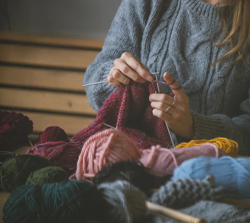 Person som strikker med fargerike garnnøster på et bord, koselig høststemning.